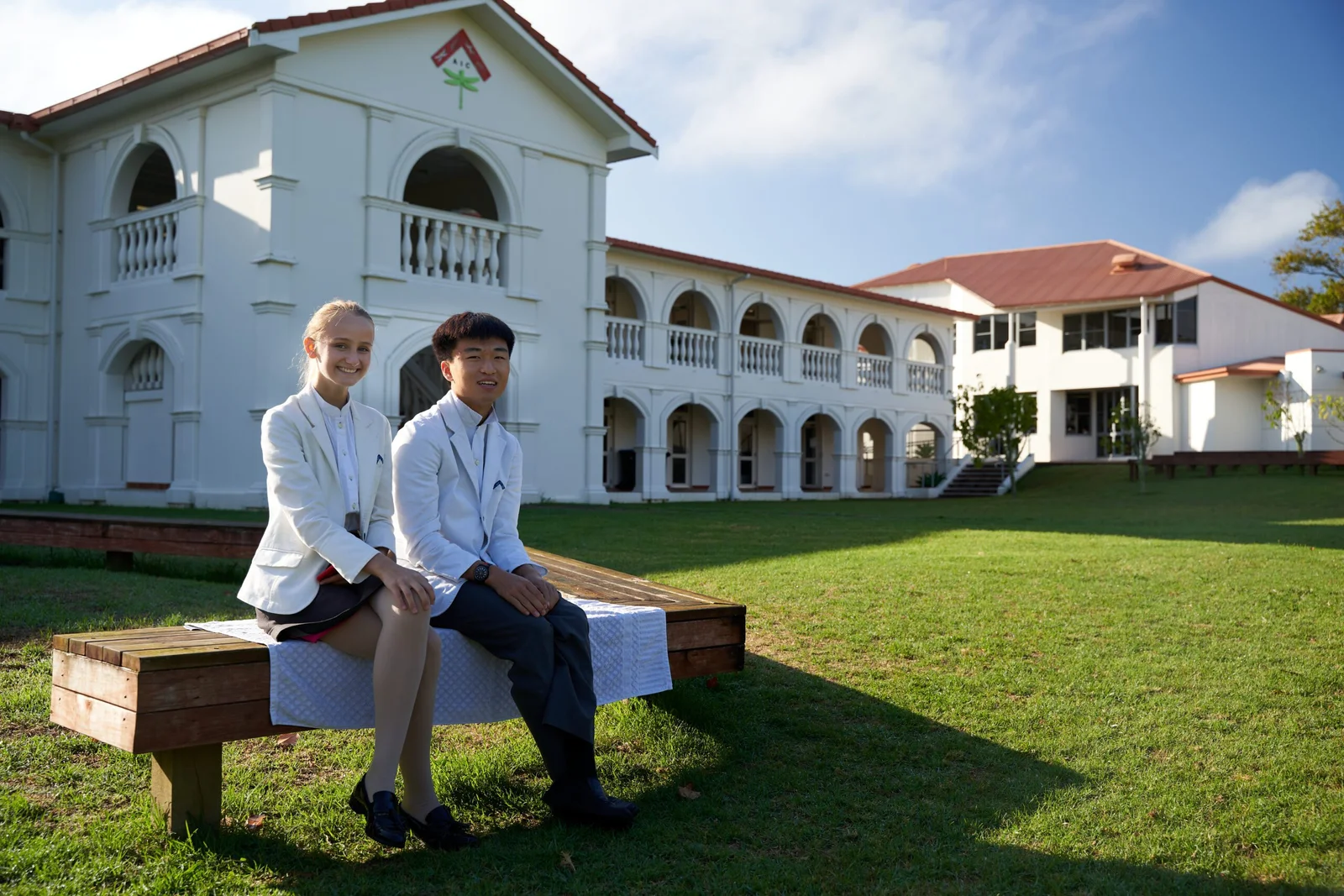 Young man and woman in school uniforms sitting on a wooden bench