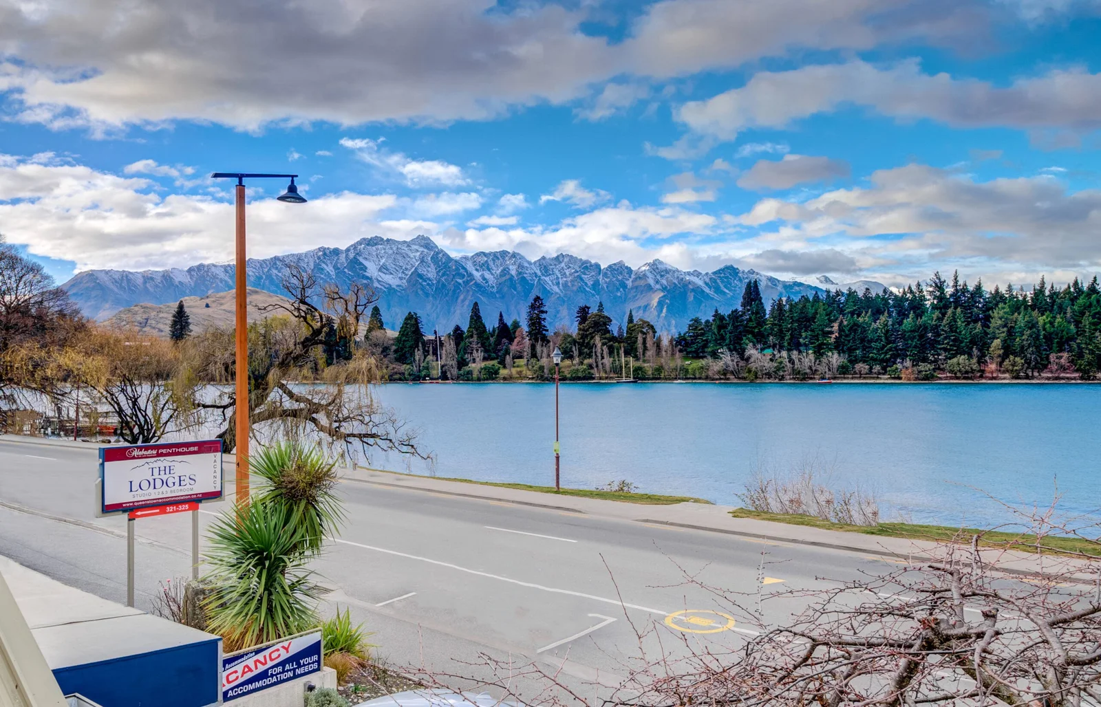 Scenic lakeside view with mountains and The Lodges sign in Queenstown