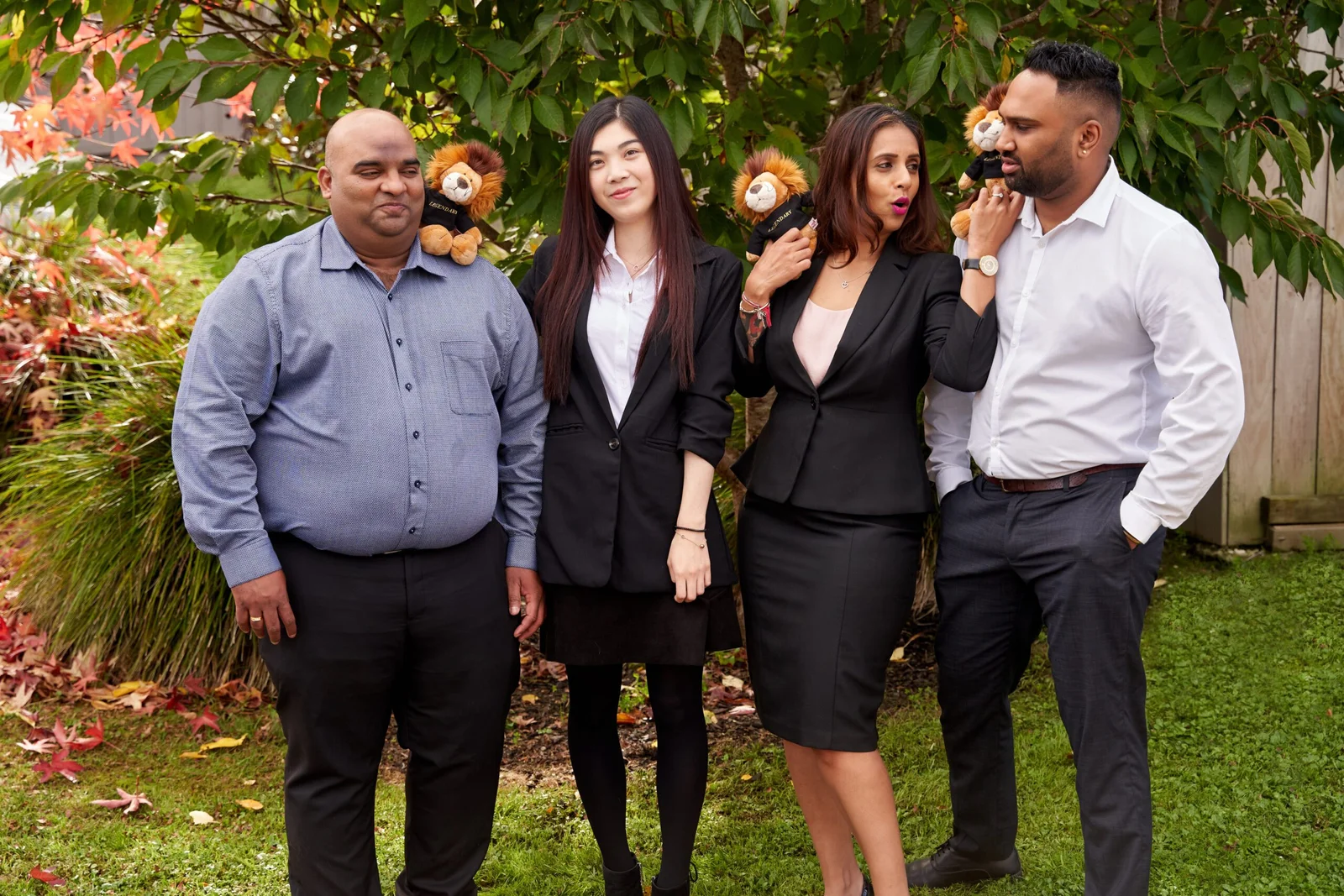 Four business professionals in suits holding lion mascots in garden setting