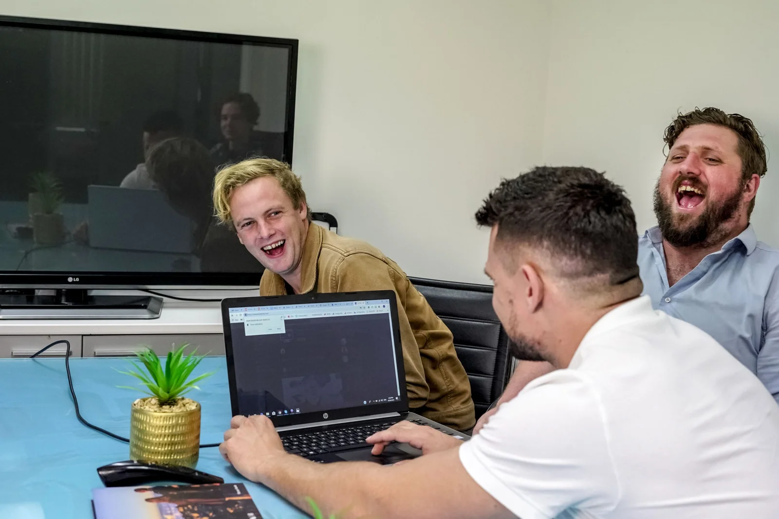 Three men laughing and collaborating at laptop in modern office setting