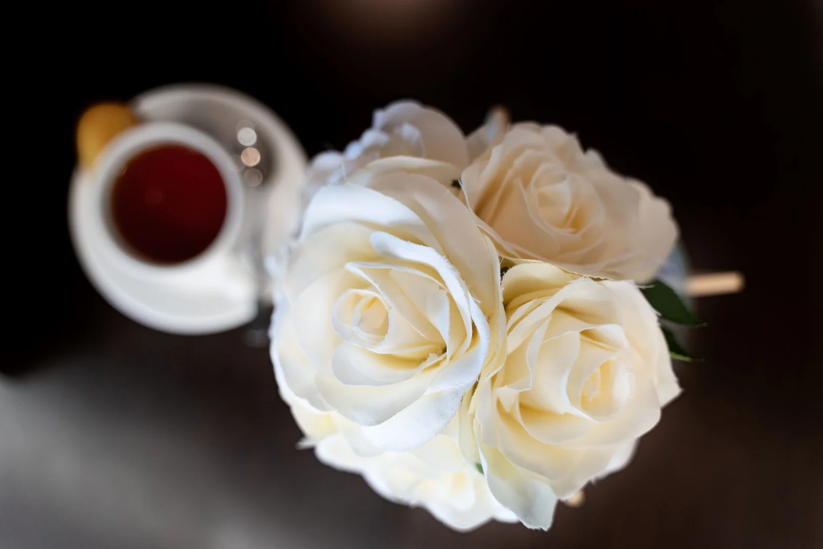 White roses arranged next to cup of tea on dark surface
