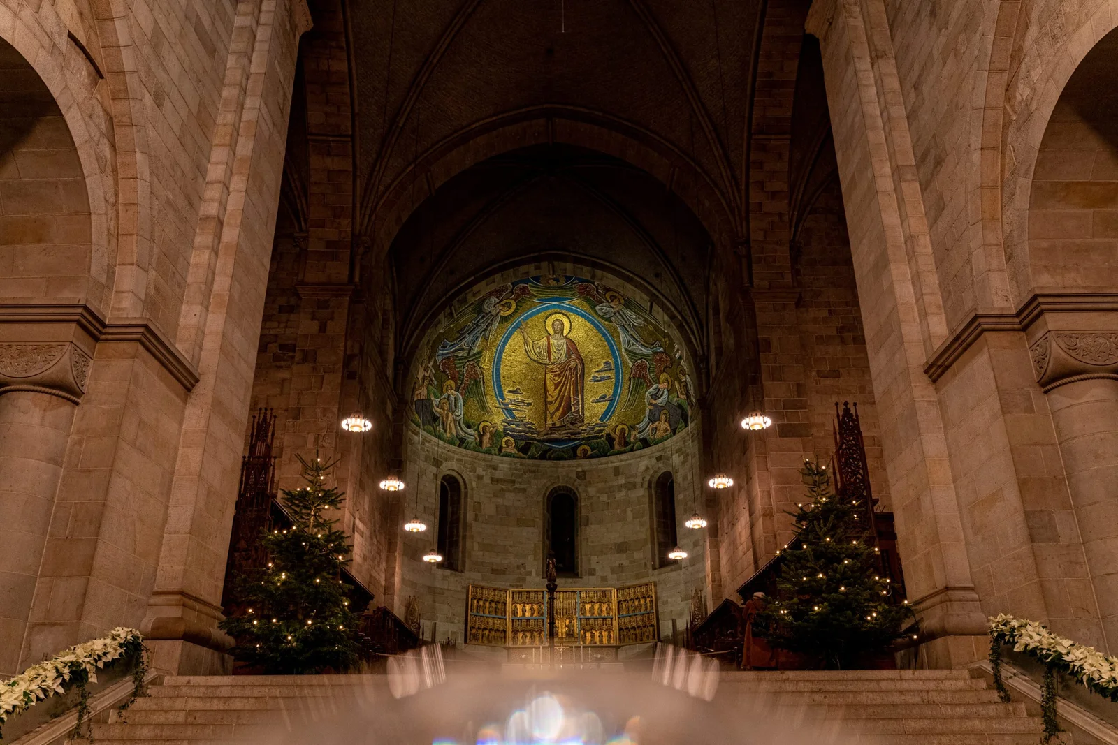 Interior of a grand church with a large mosaic depicting a religious figure, adorned with Christmas trees and lights