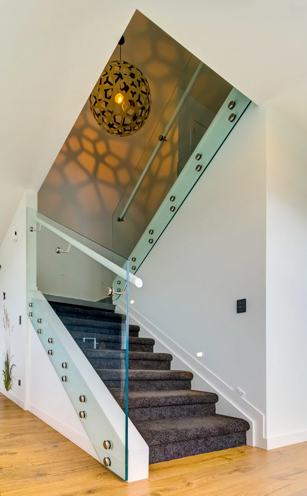 Modern staircase with glass railings and dark carpeted steps, featuring a decorative spherical light fixture casting a patterned shadow on the wall