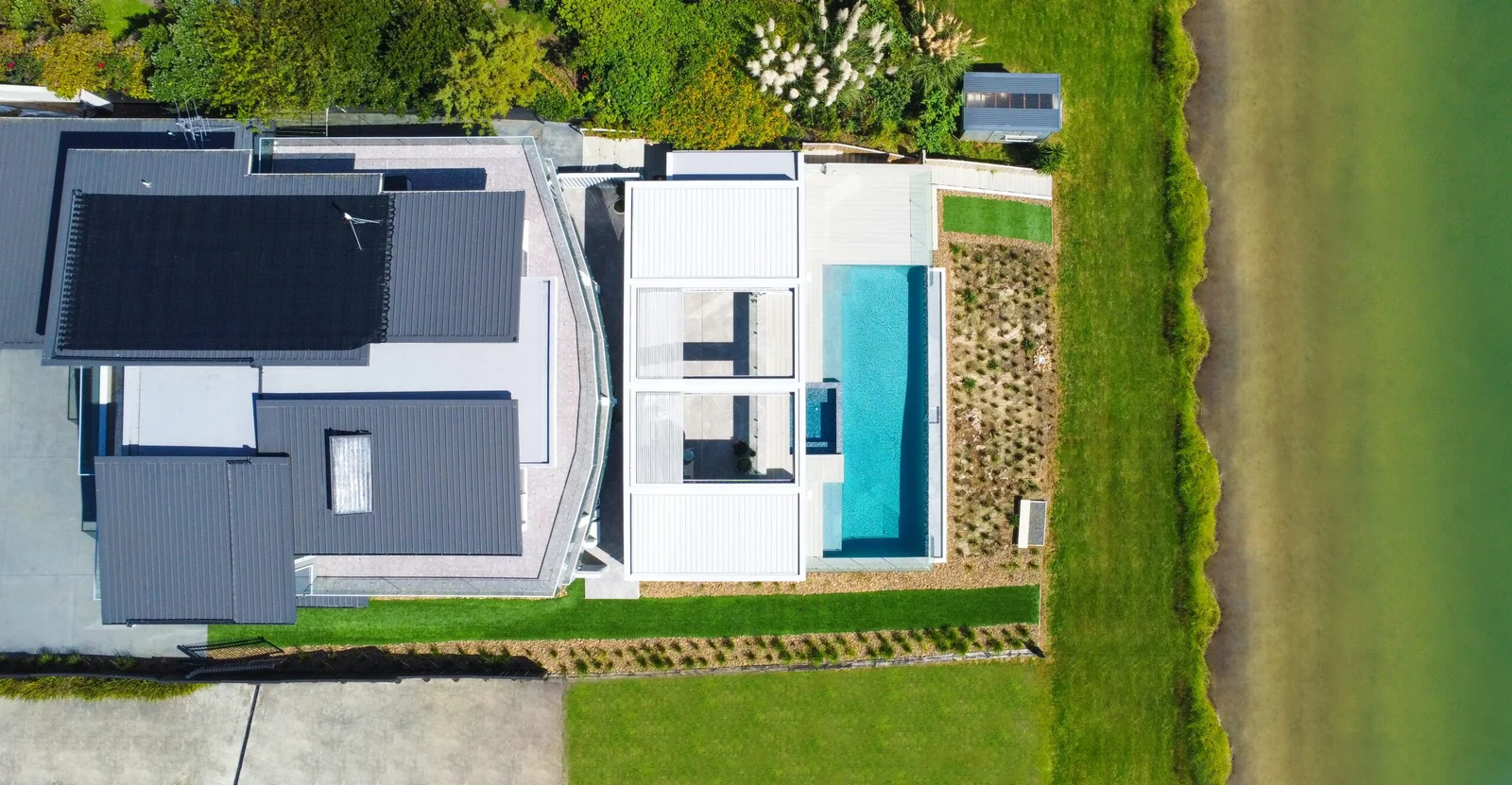 An aerial view of a modern house with a swimming pool and landscaped garden next to a body of water