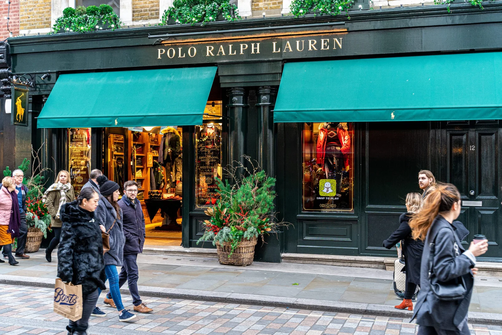 Street view of a Polo Ralph Lauren store with a green awning, showing people walking by and Christmas decorations