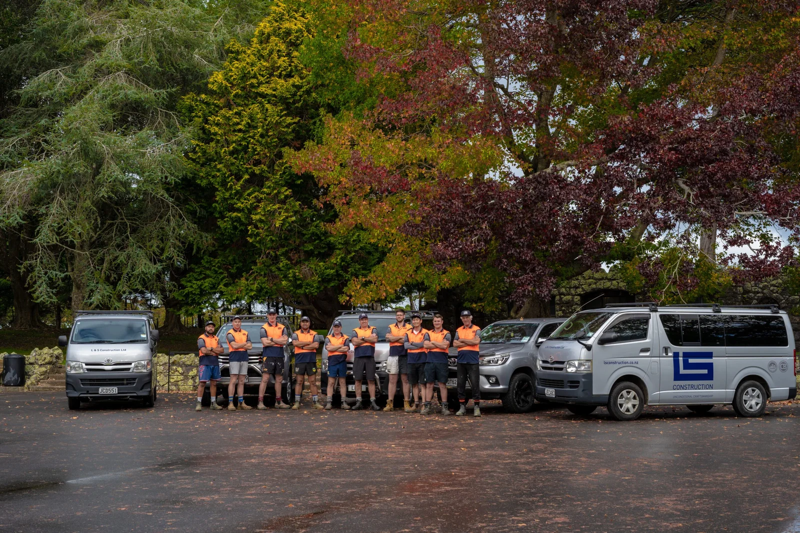 Group of construction workers in orange high-vis gear with work vehicles