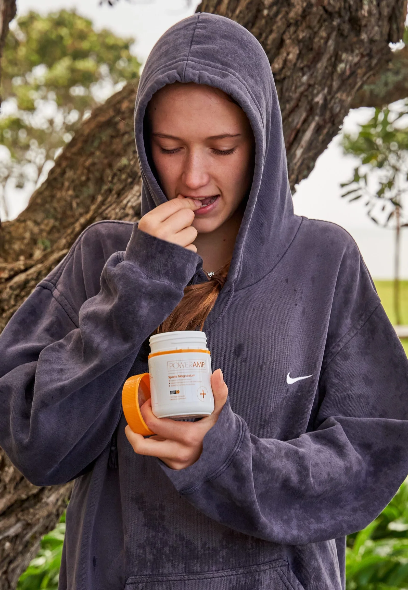 Young woman in Nike hoodie taking PowerAmp supplement outdoors