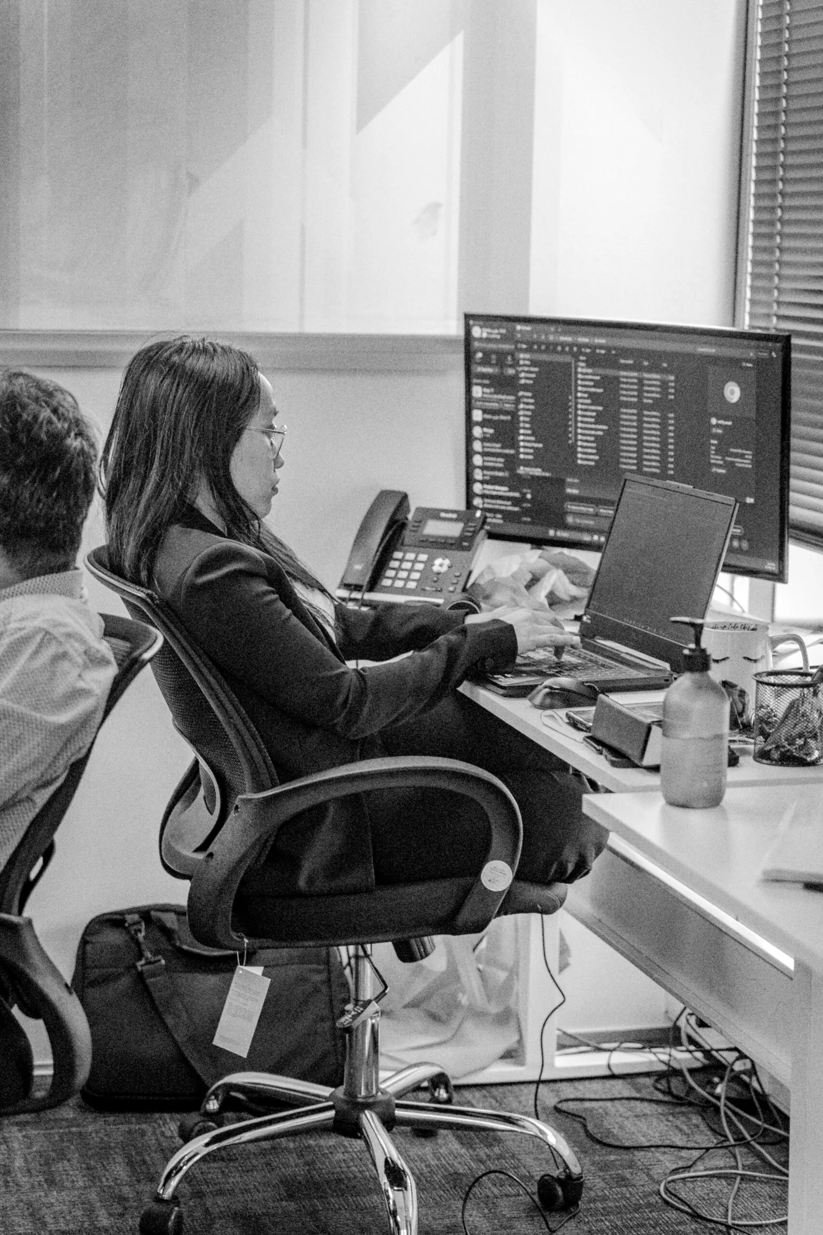 Woman working on a laptop at an office desk (black and white)