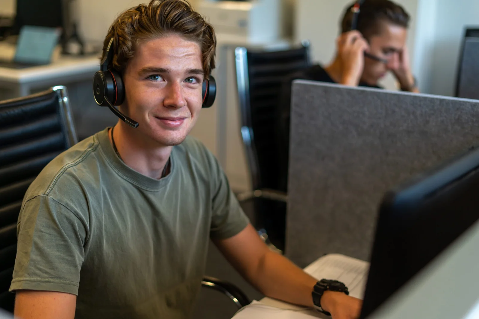 Young man with headset smiling at camera in an office