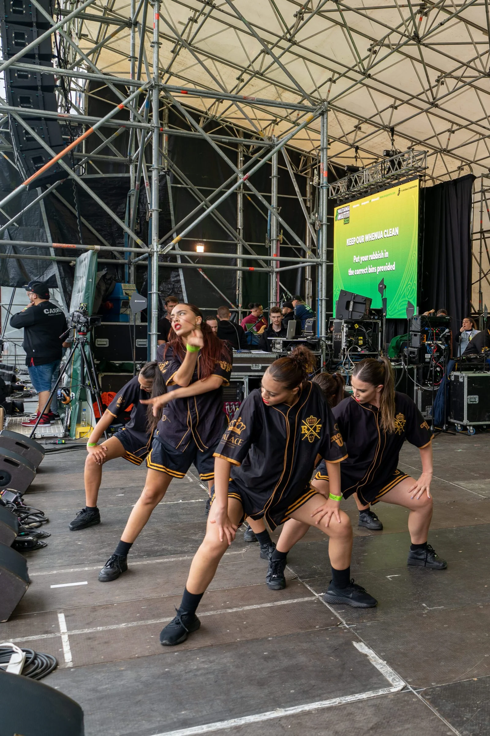 Female dancers in black and gold outfits performing on an outdoor stage