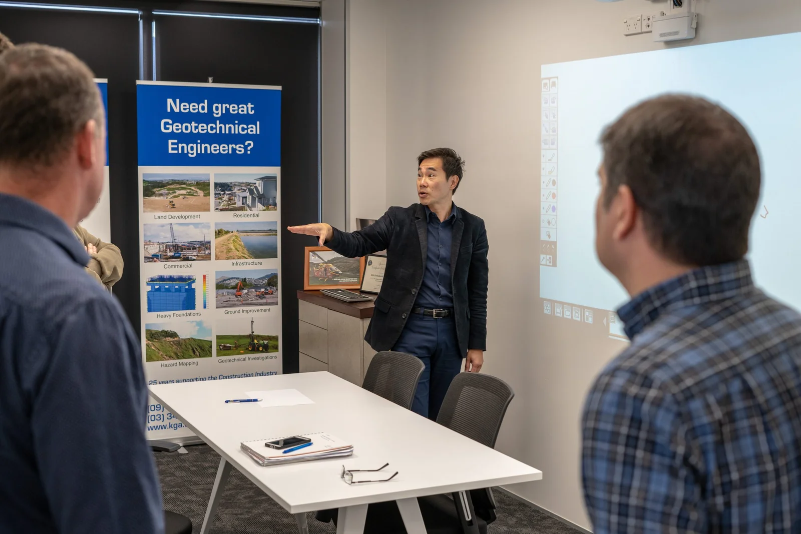 Man presenting in a meeting room with 'Need great Geotechnical Engineers?' banner